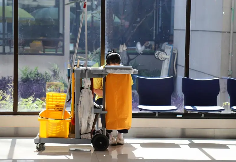 a woman in a yellow robe and a cart with a bucket and a mop